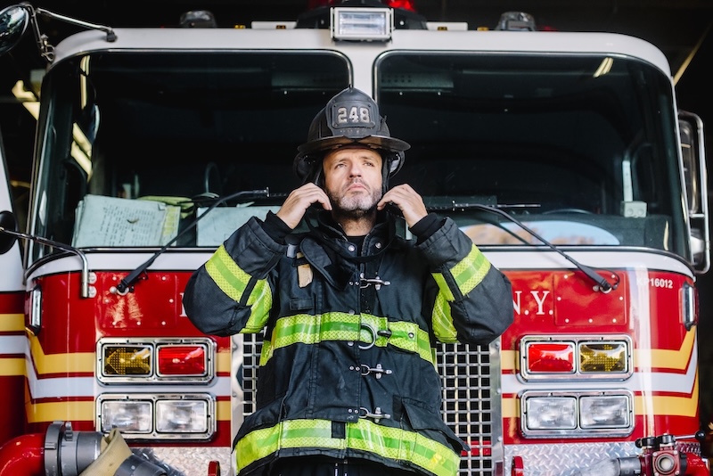 Firefighter in front of fire truck in firefighting gear.